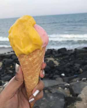 a woman holds a gelato against the backdrop of waves crashing on the rocks on Pondicherry's promenade beach and walking with an ice cream in Pondicherry beach