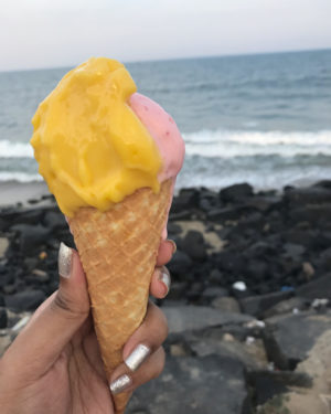 a woman holds a gelato against the backdrop of waves crashing on the rocks on Pondicherry's promenade beach